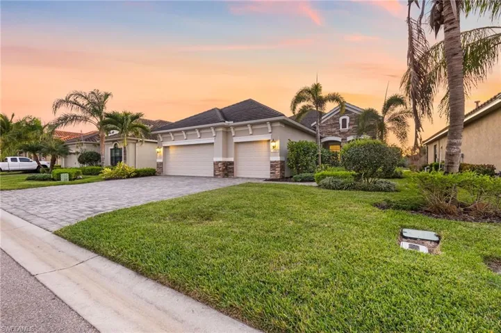 View of front of property featuring a yard, an attached garage, stucco siding, stone siding, and decorative driveway