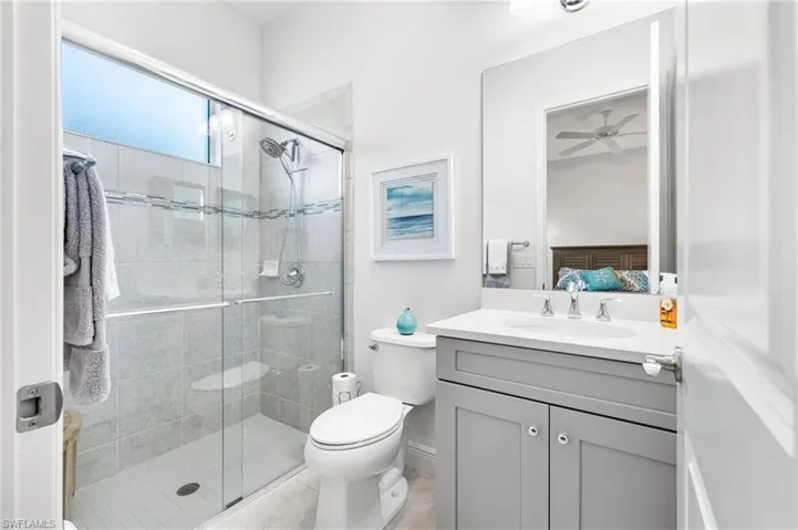 Ensuite bathroom with toilet, a stall shower, ensuite bathroom, vanity, and a ceiling fan