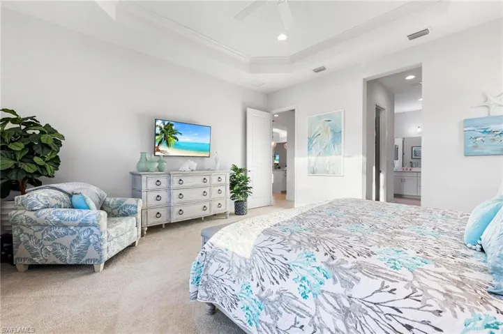 Carpeted bedroom with visible vents, a tray ceiling, ornamental molding, recessed lighting, and ensuite bathroom