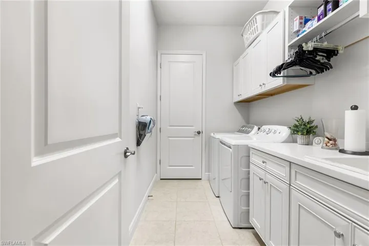 Laundry room featuring baseboards, cabinet space, light tile patterned flooring, and washing machine and clothes dryer