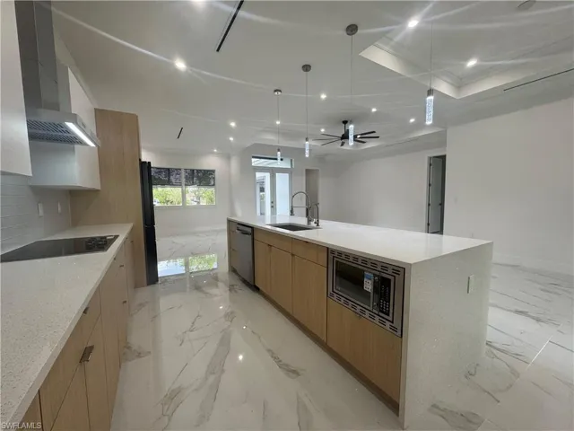 Kitchen with a spacious island,  appliances, and a Kitchen featuring light brown cabinetry, dishwasher, sink, and a raised ceiling, microwave.