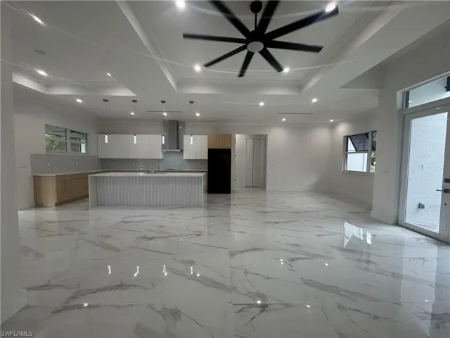 Unfurnished living room featuring ceiling fan, pantry closet, marble finish floor, a tray ceiling, and recessed lighting