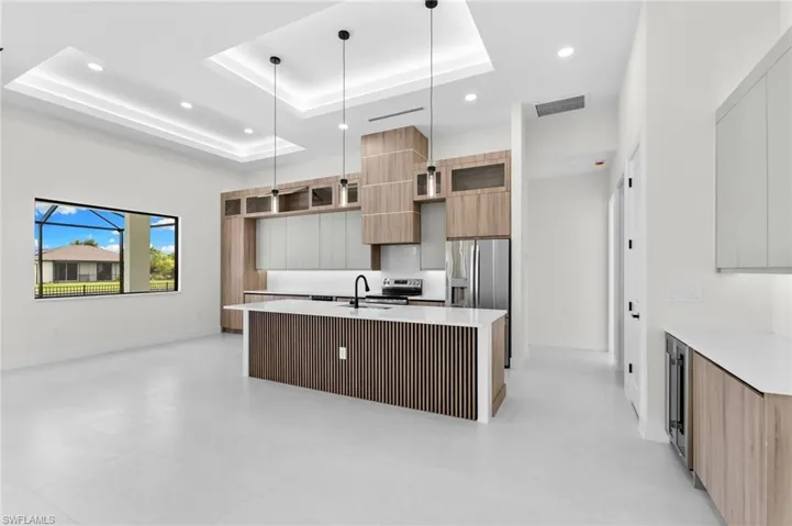 Recessed and tray ceiling lighting, stainless steel appliances, wood-finish cabinetry, and a kitchen island with a slatted wood-finish base