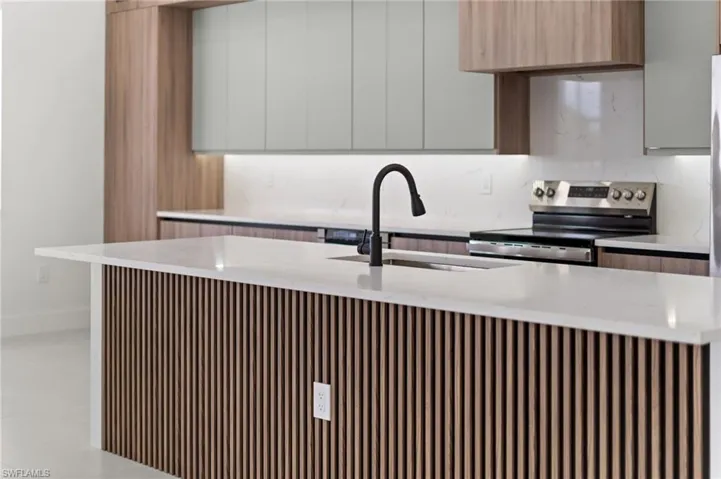 Kitchen island with slatted wood-finish paneling, white countertop, integrated sink, and matte black faucet