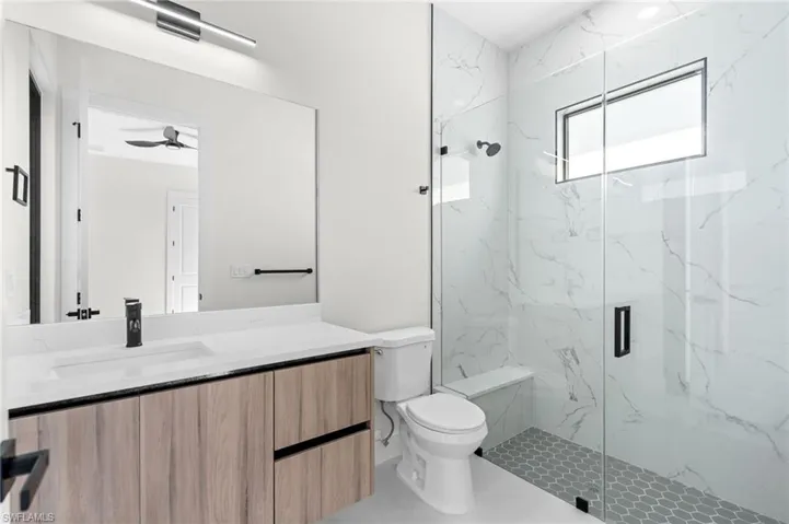 Spacious bathroom featuring a frameless glass shower enclosure, wood-finish vanity with an integrated sink, and large format mirror