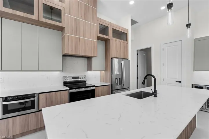 Kitchen featuring a large island with an undermount sink, a stainless steel refrigerator, built-in microwave, and wood-finish cabinetry