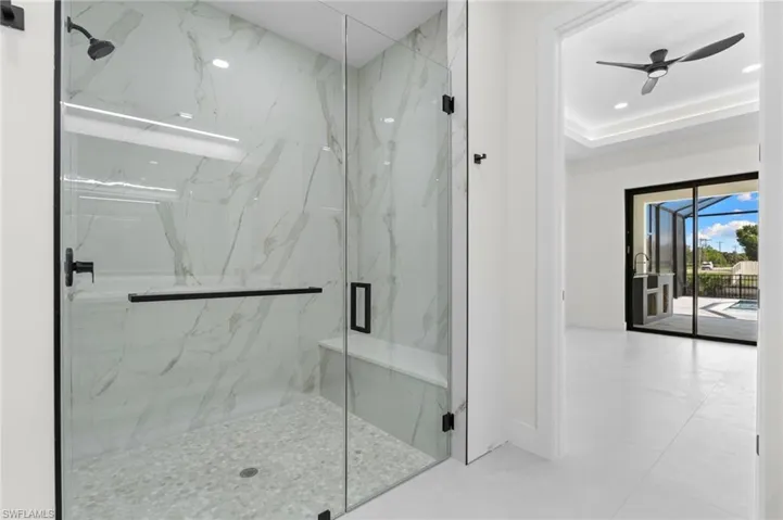 Glass-enclosed shower with a built-in bench, marble-patterned wall tile, and matte black fixtures