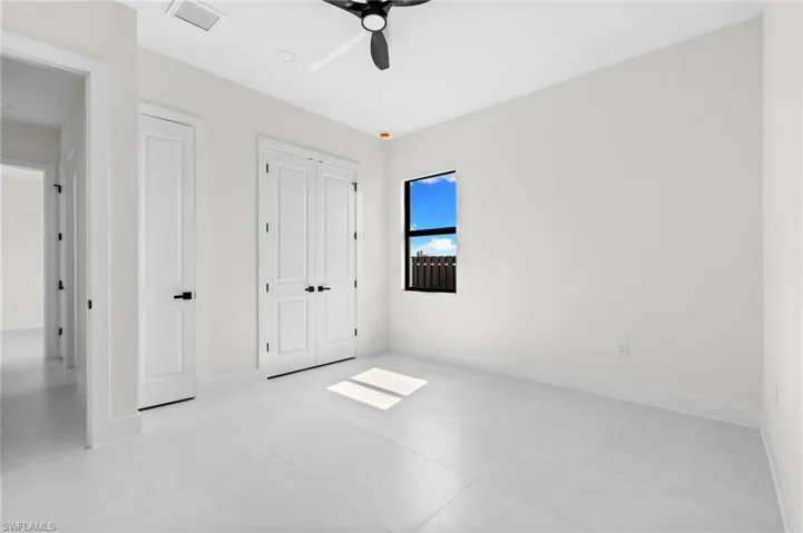 White tiled flooring, dual panel doors with matte black hardware, single window with dark frame, white walls, and a black ceiling fan