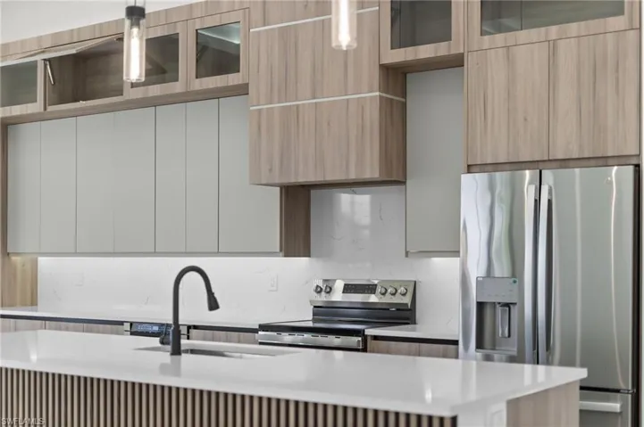 Kitchen featuring two-tone cabinetry with wood-finish and light gray doors, white countertops, a matte black gooseneck faucet, and stainless steel appliances