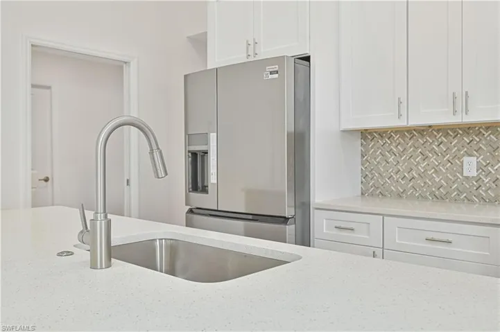 Kitchen featuring white cabinetry, stainless steel fridge, light stone countertops, and backsplash