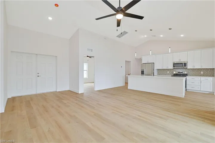 Kitchen featuring open floor plan, white cabinetry, light countertops, stainless steel appliances, and a center island with sink