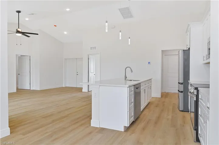 Kitchen featuring white cabinets, a center island with sink, light wood-style floors, stainless steel appliances, and vaulted ceiling