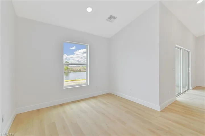 Dining room with vaulted ceiling, light wood-type flooring, a water view, and recessed lighting