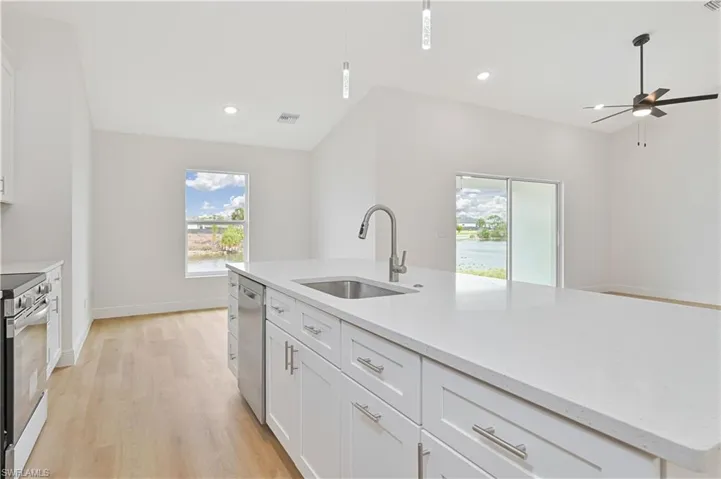 Kitchen featuring white cabinetry, a center island with sink, light stone countertops, a ceiling fan, and light wood-style flooring