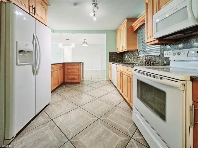 Kitchen with white appliances, a peninsula, tasteful backsplash, hanging light fixtures, and dark stone countertops