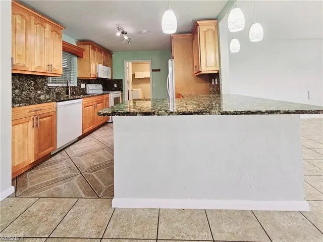 Kitchen with dark stone counters, white appliances, pendant lighting, a peninsula, and backsplash