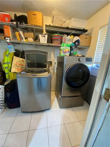 Clothes washing area with separate washer and dryer, light tile patterned floors, and a textured ceiling