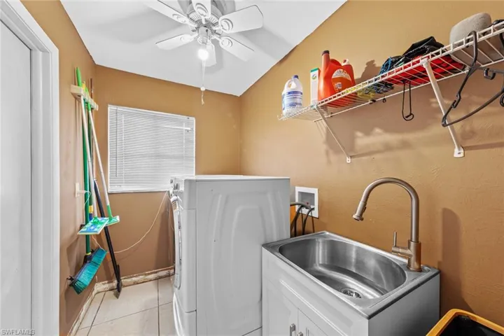 Washroom featuring light tile patterned floors, hookup for a washing machine, sink, cabinets, and ceiling fan