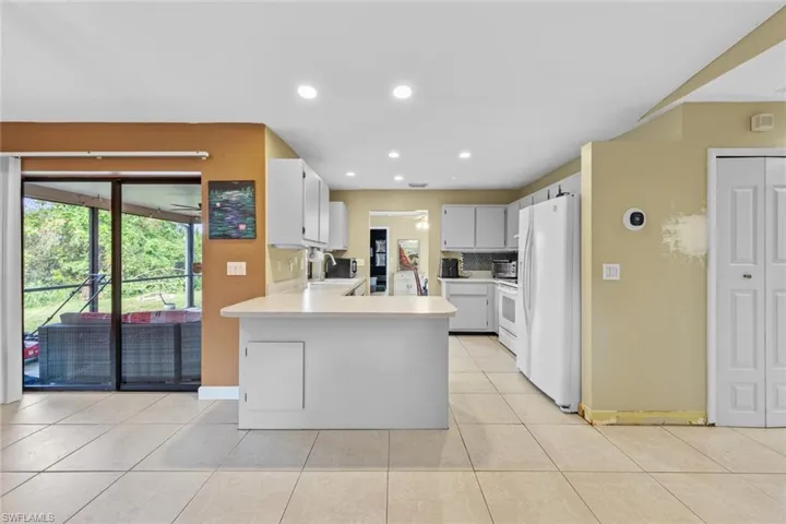 Kitchen bar seating/peninsula sink, light tile patterned flooring, white cabinets, and white appliances
