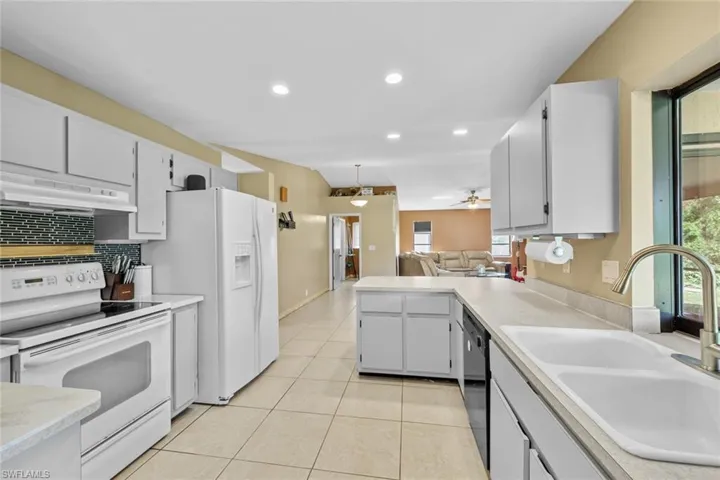 Kitchen with sink, light tile patterned flooring, white cabinets, white appliances, and ceiling fan