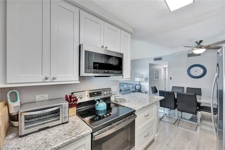 Kitchen featuring stainless steel appliances, a textured ceiling, open floor plan, white cabinets, and a ceiling fan
