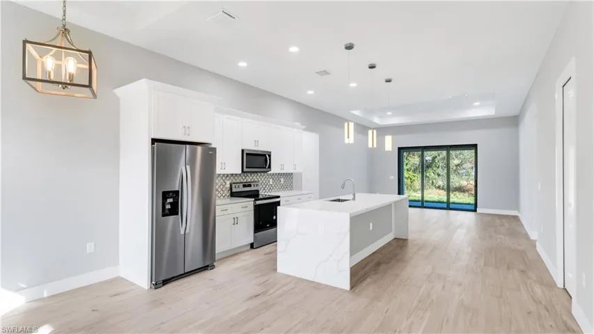 Kitchen featuring pendant lighting, appliances with stainless steel finishes, a raised ceiling, white cabinets, and recessed lighting
