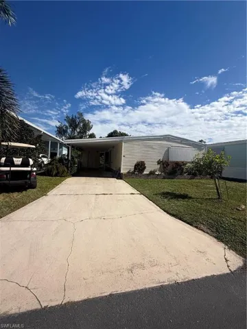 Manufactured / mobile home featuring concrete driveway, a front lawn, and an attached carport