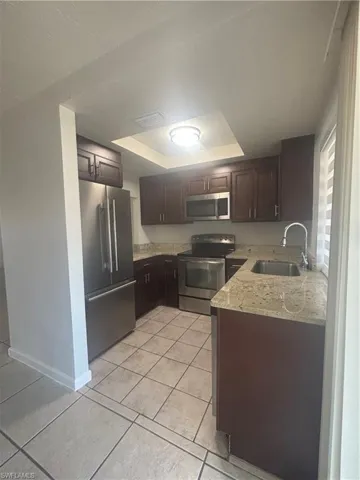 Kitchen featuring light stone counters, stainless steel appliances, dark wood finish cabinets, a tray ceiling, and light tile patterned flooring