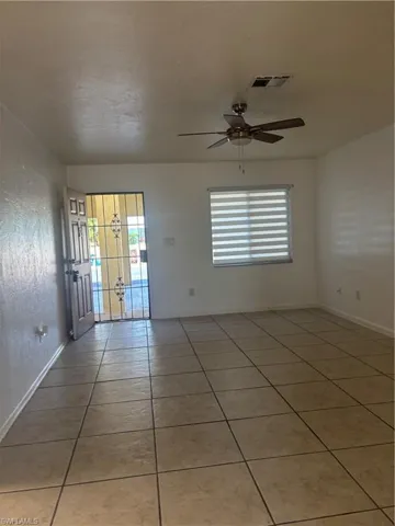 Empty room featuring light tile patterned floors, ceiling fan, and healthy amount of natural light