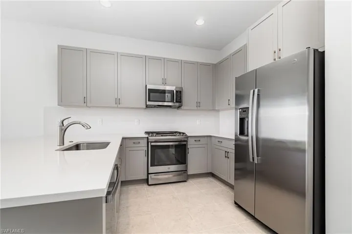 Kitchen featuring gray cabinetry, appliances with stainless steel finishes, light stone countertops, light tile patterned floors, and a peninsula