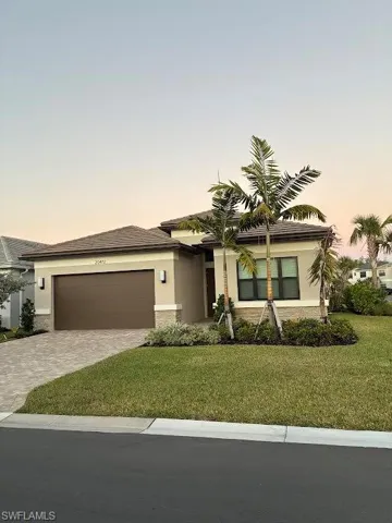 View of front of property with a yard, decorative driveway, stucco siding, and a garage