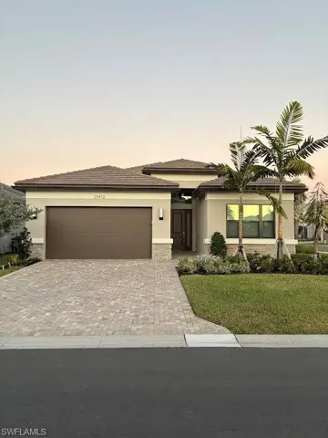 Prairie-style house with decorative driveway, stucco siding, a front lawn, an attached garage, and stone siding