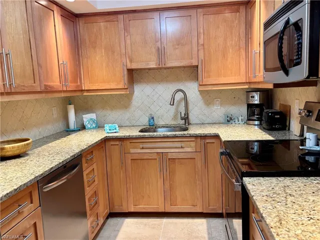 Kitchen with backsplash, light stone counters, sink, and stainless steel appliances
