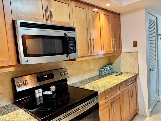 Kitchen featuring tasteful backsplash, light stone counters, and appliances with stainless steel finishes
