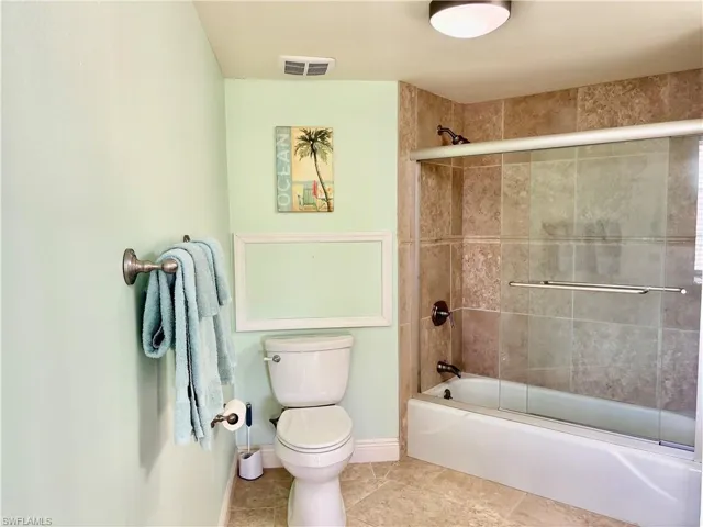 Bathroom with shower / bath combination with glass door, tile patterned floors, and toilet