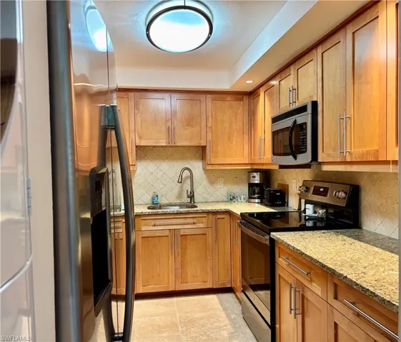 Kitchen featuring tasteful backsplash, light stone countertops, sink, and appliances with stainless steel finishes