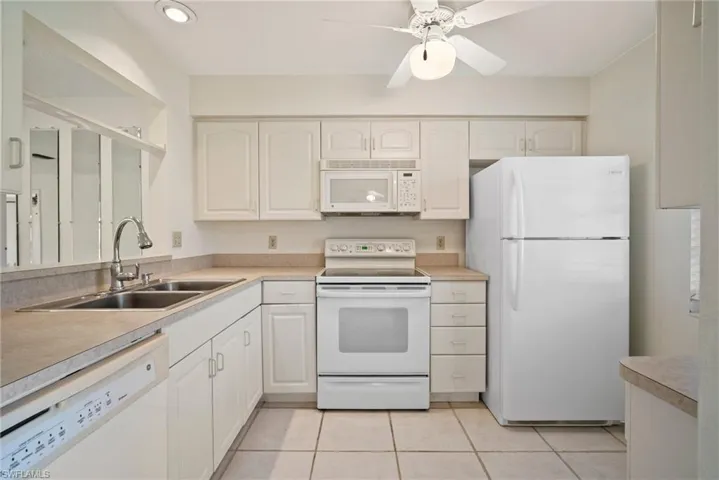 Kitchen featuring sink, white cabinetry, white appliances, and light tile patterned flooring