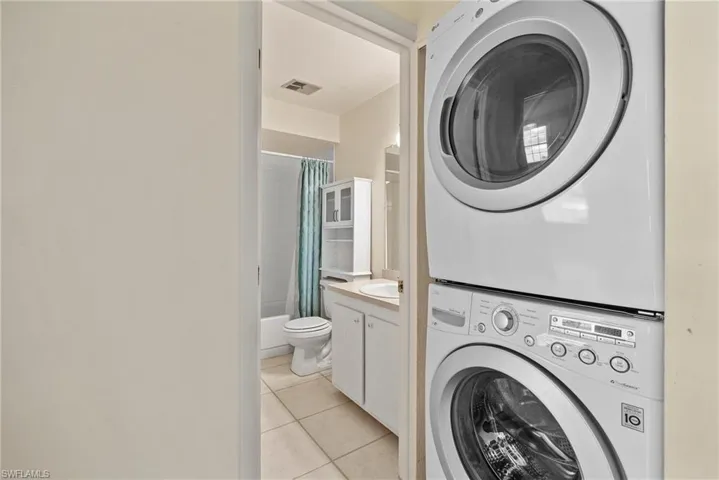 Clothes washing area featuring light tile patterned flooring and stacked washer and clothes dryer