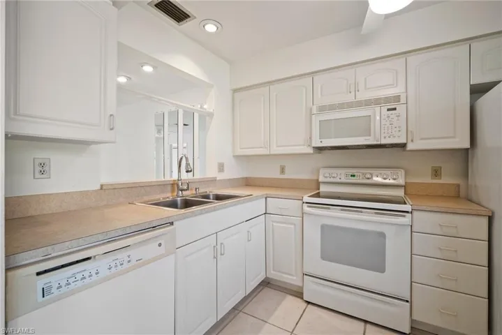 Kitchen featuring sink, white cabinets, white appliances, and light tile patterned flooring