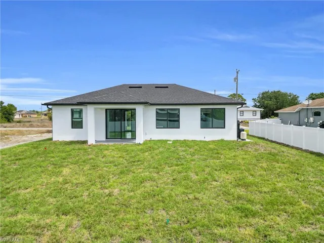 Rear view of property featuring stucco siding, roof with shingles, fence, and a yard