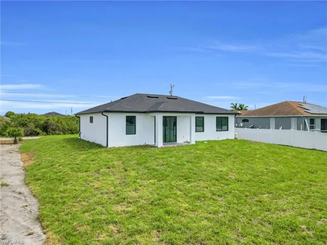 Back of property with a lawn, roof with shingles, fence, and stucco siding