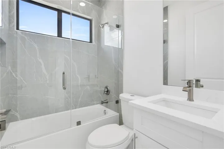 Bathroom featuring vanity, enclosed tub / shower combo, and toilet