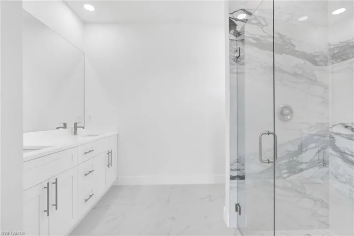Full bath with a sink, double vanity, a marble finish shower, marble finish floor, and baseboards