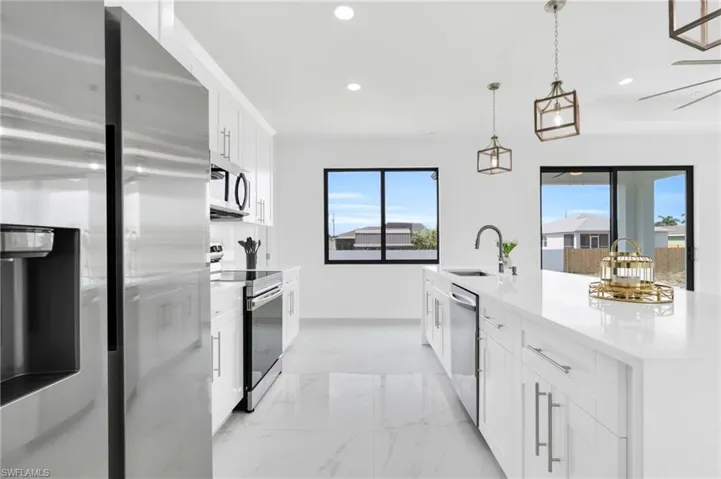 Kitchen with appliances with stainless steel finishes, hanging light fixtures, a sink, white cabinets, and recessed lighting