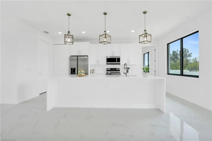 Kitchen with a kitchen island with sink, appliances with stainless steel finishes, white cabinets, marble finish floor, and recessed lighting