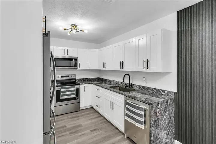 Kitchen featuring dark stone countertops, appliances with stainless steel finishes, white cabinets, a textured ceiling, and light wood-type flooring