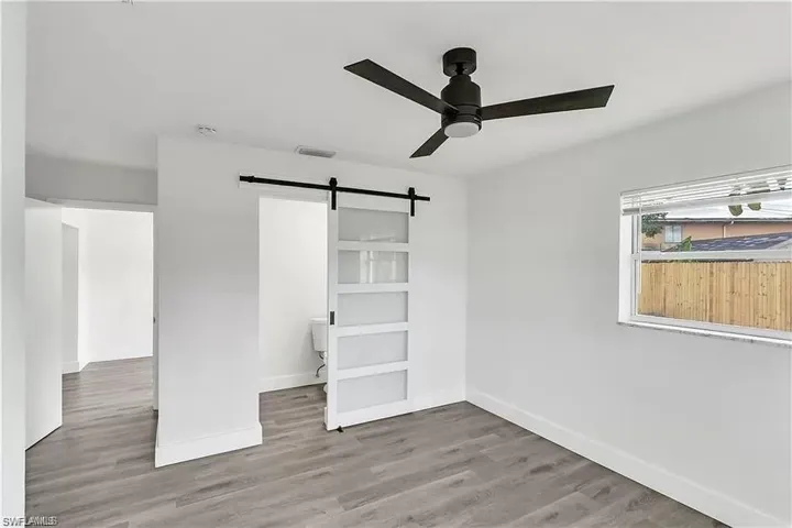 Unfurnished bedroom with a barn door, light wood finished floors, and ceiling fan