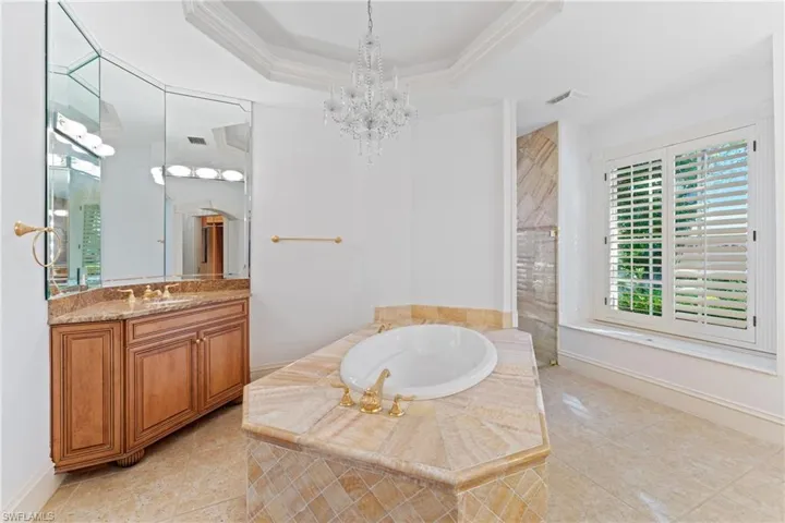 Bathroom featuring a raised ceiling, crown molding, a chandelier, shower with separate bathtub, and vanity