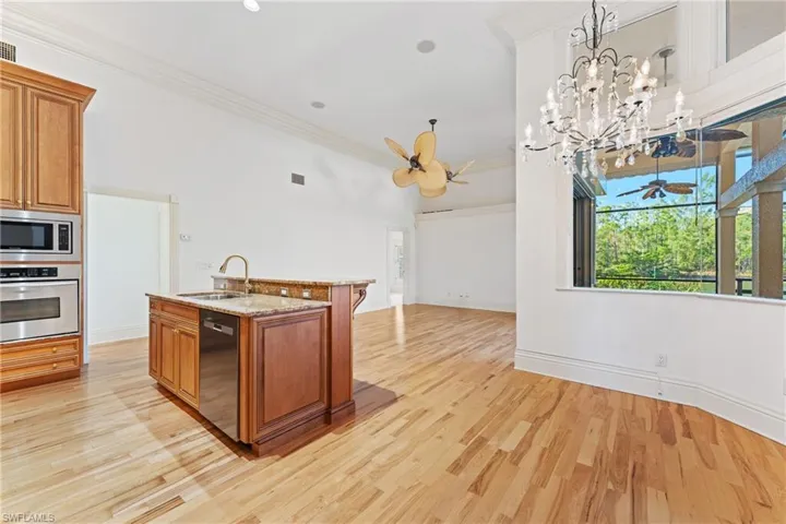 Kitchen with ceiling fan with notable chandelier, stainless steel appliances, sink, hanging light fixtures, and an island with sink