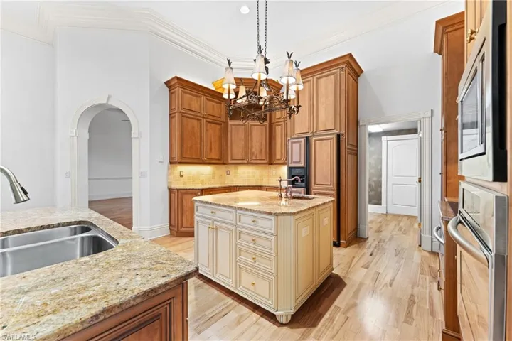 Kitchen with pendant lighting, sink, light stone countertops, an island with sink, and appliances with stainless steel finishes